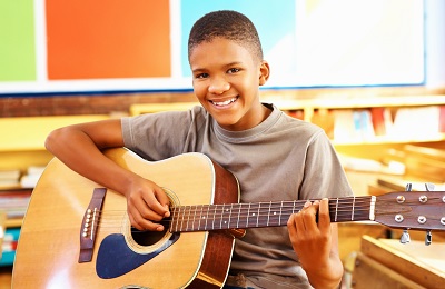 child with a smile holding a 
            guitar